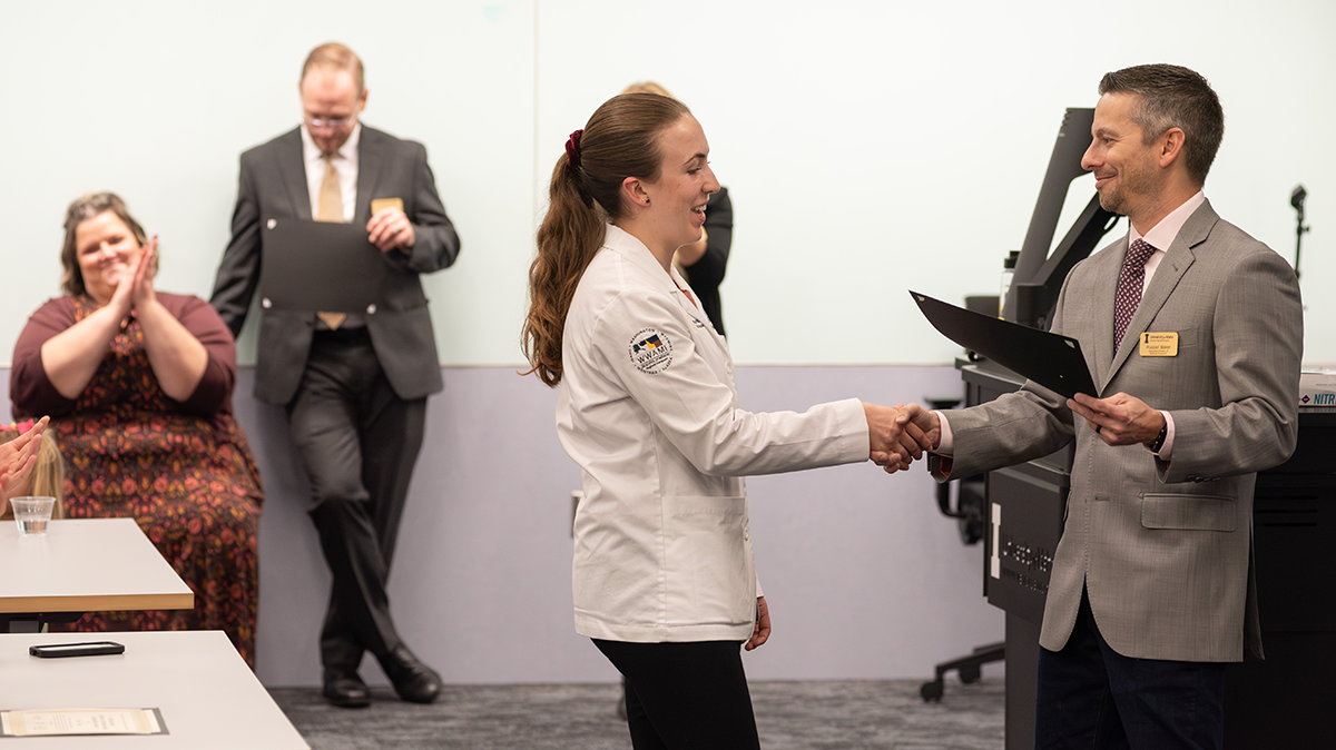 Female student shakes the hand of the man presenting her with an award.
